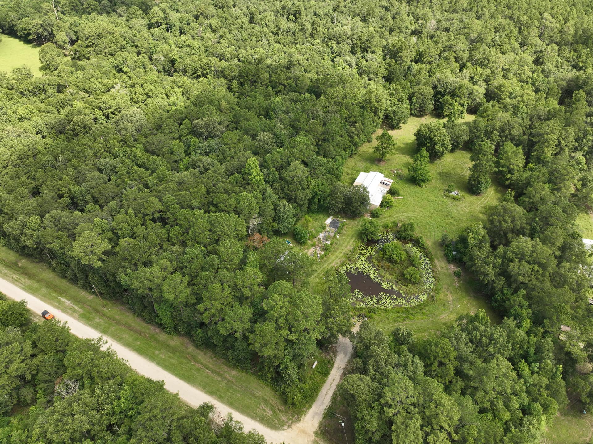 Aerial drone photo of wooded acreage with a clearing and pond on County Road 126, Liberty County, Texas